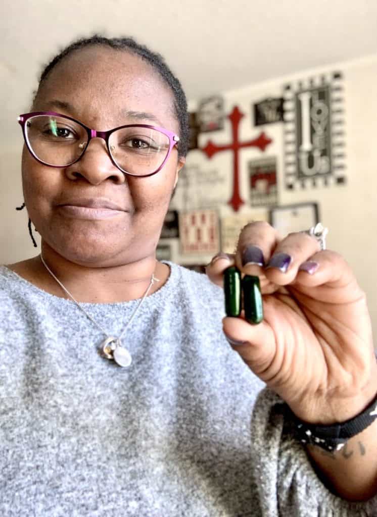 Woman smiling and holding 2 green capsules. They are the Daily Seed Synbiotic.